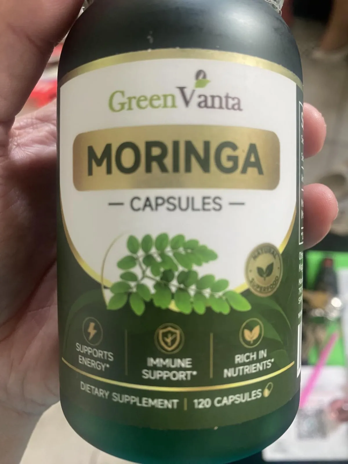 Hand holding the GREENVANTA Moringa Capsules bottle showing the front label