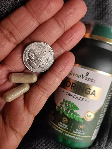 Two GREENVANTA moringa capsules in a hand next to a US quarter for size comparison