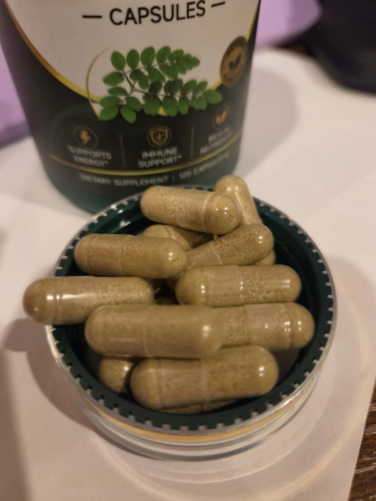 Close-up of green-brown moringa leaf powder capsules in the GREENVANTA bottle cap